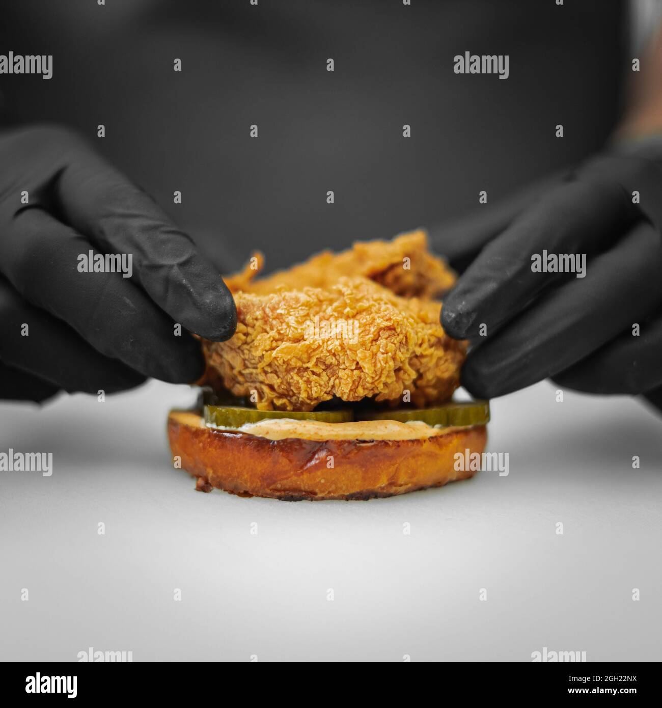 Gros plan d'un cuisinier plaçant des nuggets de poulet sur les cornichons en tranches tout en superposant un hamburger Banque D'Images
