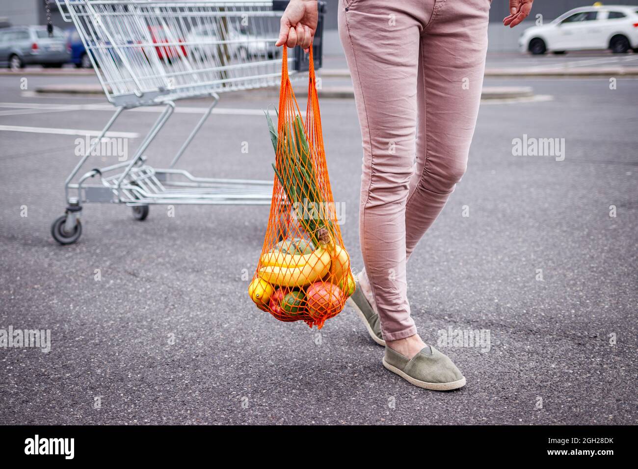 Femme avec sac en filet réutilisable marchant du chariot dans le parking à côté du supermarché. Concept sans plastique et sans déchets. Achat d'articles d'épicerie Banque D'Images
