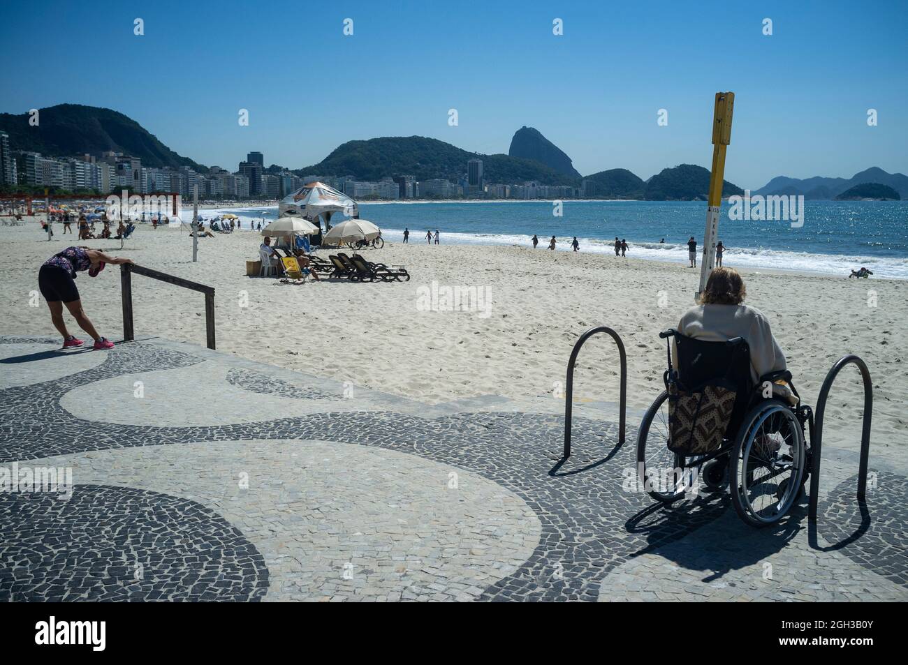 Une femme âgée handicapée en fauteuil roulant bénéficie de la vue sur la plage de Copacabana aux côtés d'une jeune femme qui fait de l'exercice. Banque D'Images