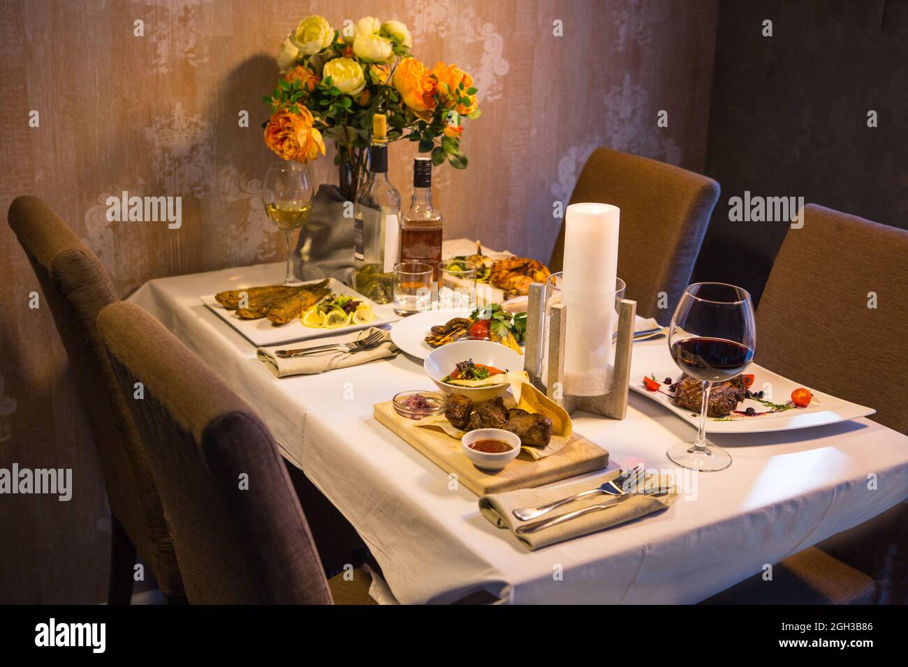 Table servie avec des plats de viande, poulet et poisson avec vin et whisky. Dîner romantique aux chandelles au restaurant Banque D'Images