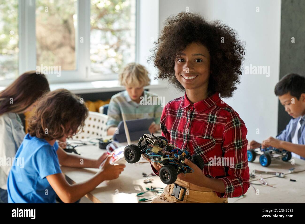 Bonne fille afro-américaine d'école de gamin tenant une voiture robotique à la classe STEM. Banque D'Images