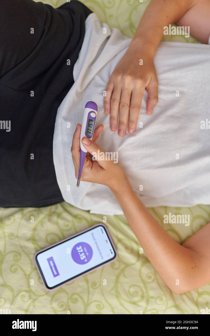 Vue de dessus d'une femme au lit en notant sa température de base Banque D'Images