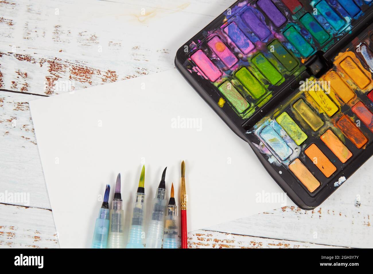 Palette de aquarelles avec des aquarelles et une feuille de papier sur une table. Concept de mise à plat. Banque D'Images