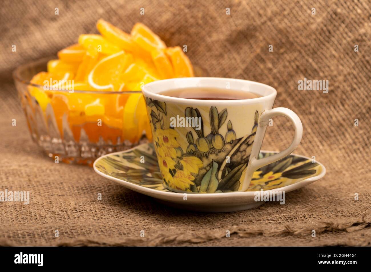 Tranches de citron marmelade multicolores dans un vase en verre et une tasse de thé sur une soucoupe, gros plan, mise au point sélective Banque D'Images
