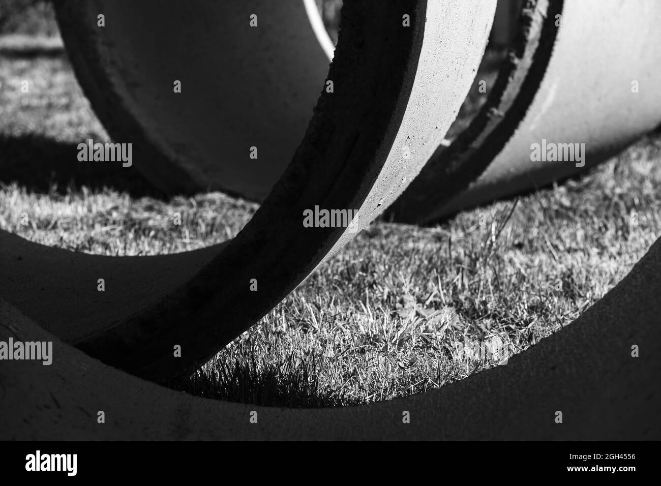 Photo en noir et blanc des détails. Des anneaux en béton reposent sur un fond photo industriel abstrait et herbacé Banque D'Images