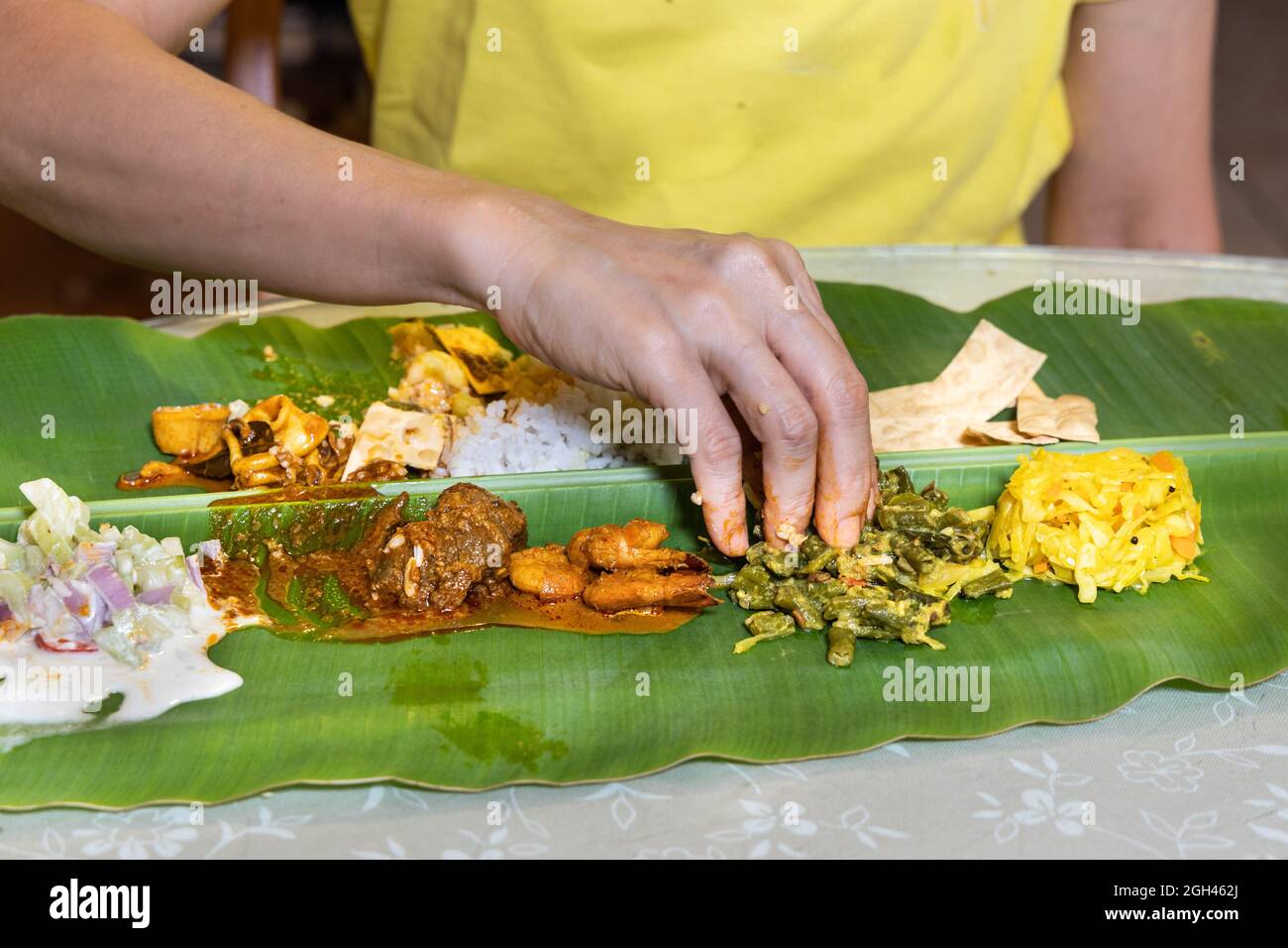 Personne appréciant le riz indien à feuilles de banane composé de curry de mouton, de calmar, de crevettes, de papapadam et de divers légumes Banque D'Images