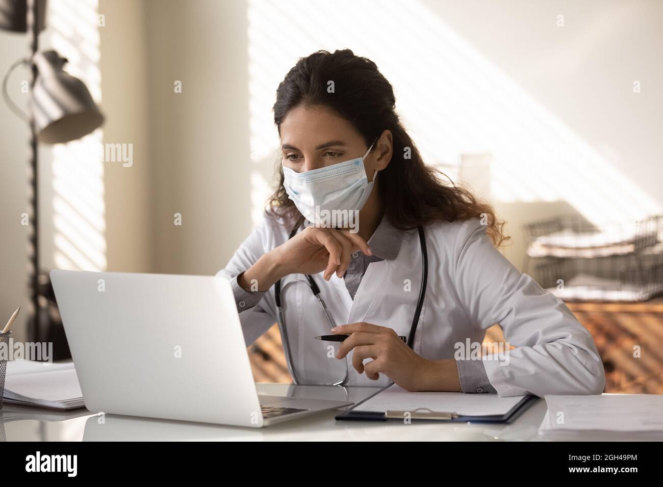 Jeune médecin généraliste en masque médical travaillant à l'ordinateur portable Banque D'Images