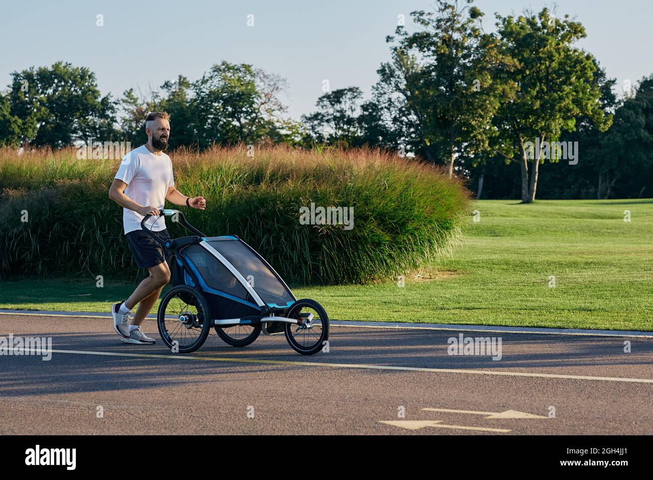 Jeune père avec son enfant dans une poussette de jogging pendant le jogging dans un parc public. Papa de la famille avec son fils pendant la course active, bonne paternité Banque D'Images