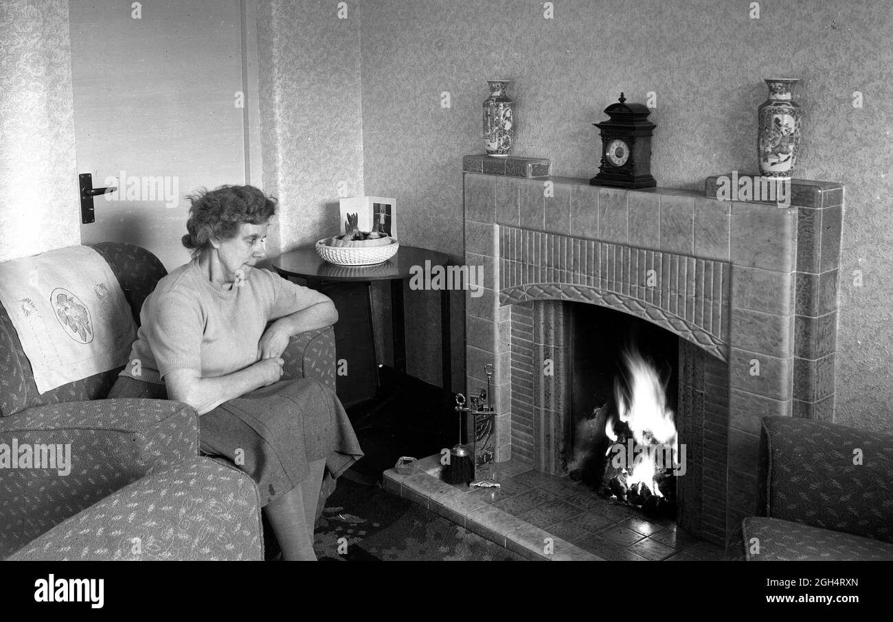 Maison douce maison âgée femme assise près de son feu de charbon dans une maison de conseil Grande-Bretagne 1952 Banque D'Images