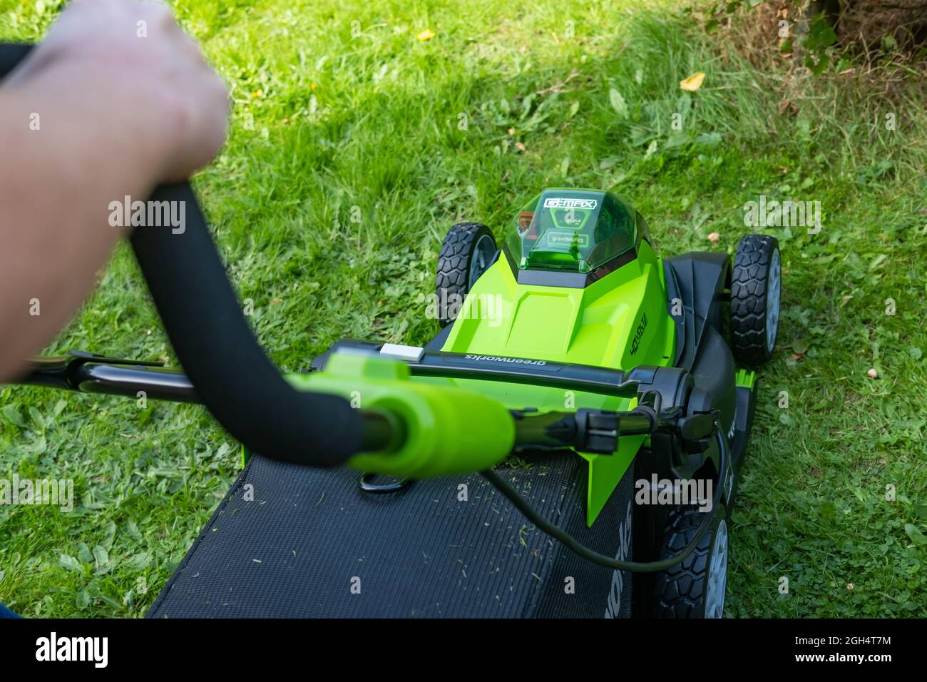 Une femme adulte non identifiable qui coupe l'herbe et tond une pelouse verte avec une tondeuse sans fil Greenworks 40v fonctionnant sur batterie. Banque D'Images