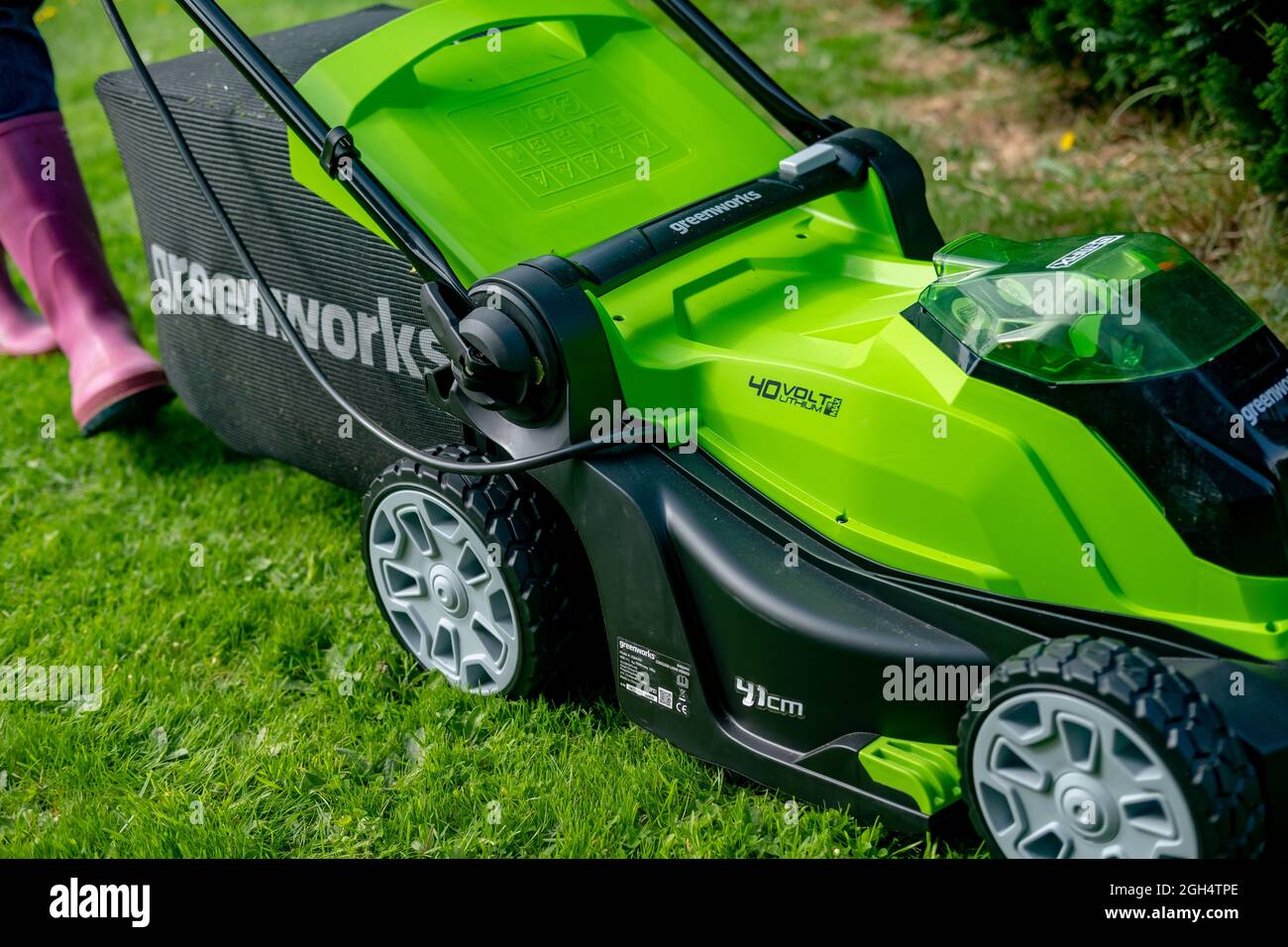 Une femme adulte non identifiable qui coupe l'herbe et tond une pelouse verte avec une tondeuse sans fil Greenworks 40v fonctionnant sur batterie. Banque D'Images