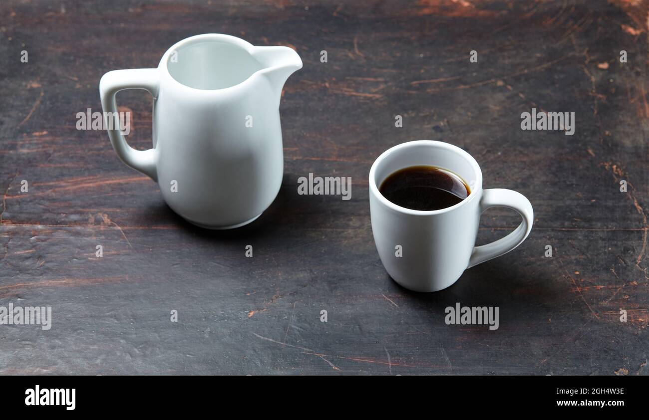 Tasse blanche avec café et pot à lait sur fond de bois blanc, gros plan. Petit déjeuner énergétique, concept de routine du matin Banque D'Images