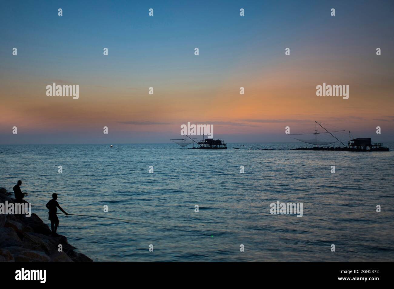 Après le coucher du soleil au port de Marina di Pisa en été . Tours de mer et de pêche, silhouettes de deux pêcheurs avec cannes à pêche Banque D'Images