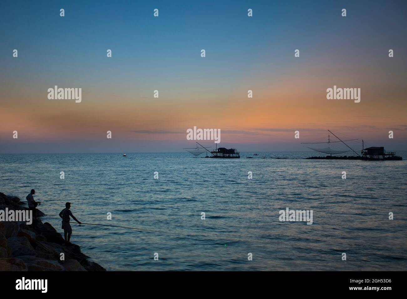 Après le coucher du soleil au port de Marina di Pisa en été . Tours de mer et de pêche, silhouettes de deux pêcheurs avec cannes à pêche Banque D'Images