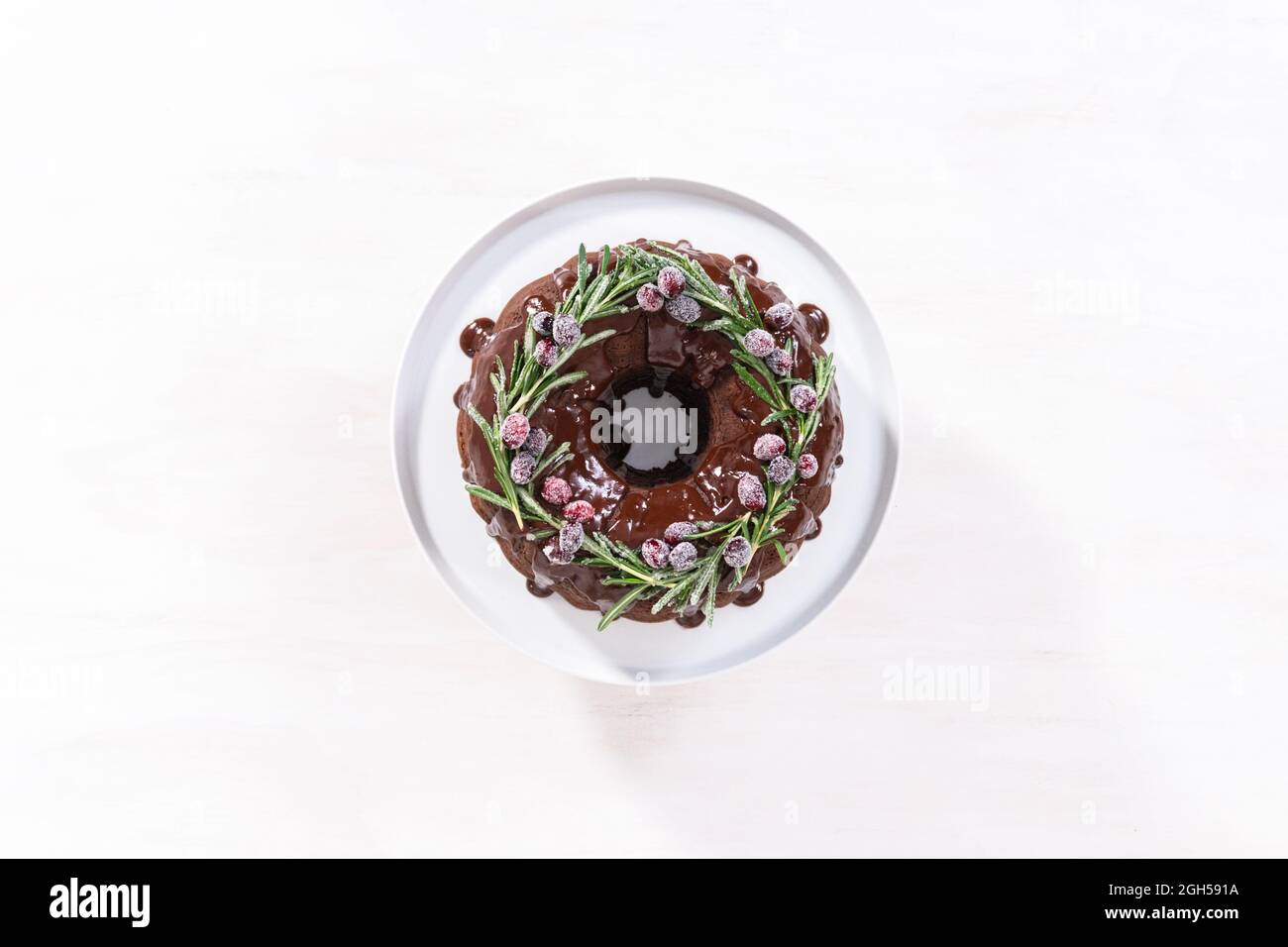 Pose à plat. Gâteau au chocolat avec glaçage au chocolat, orné de canneberges fraîches et de romarin, recouvert d'un sucre blanc. Banque D'Images