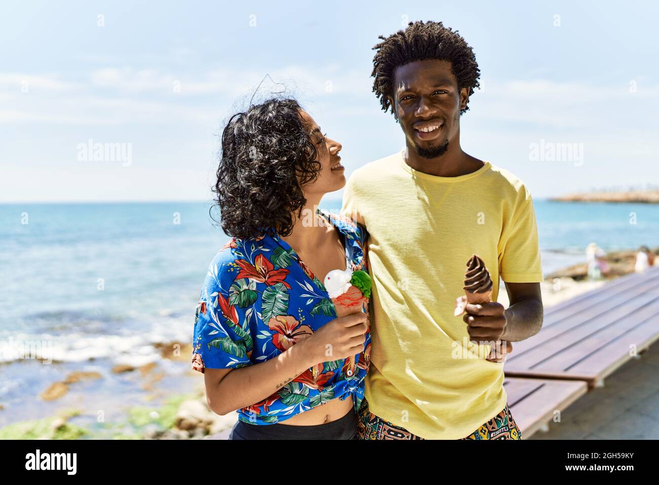 Jeune beau couple souriant heureux de manger de la glace à la plage. Banque D'Images