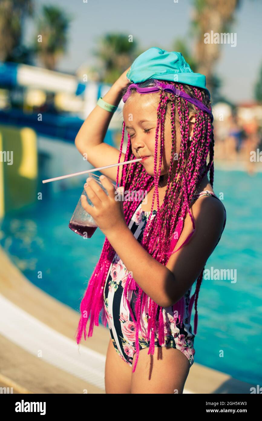 Petite fille portant un maillot de bain avec des queues de porc roses  buvant du soda au bord de la piscine Photo Stock - Alamy