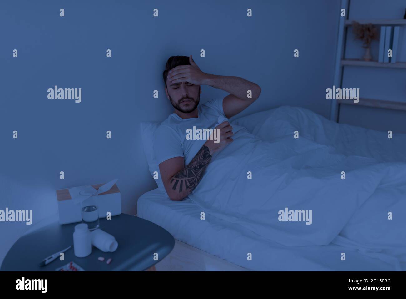 Malade gars souffrant de maux de tête et de toucher le front, se sentir mal, assis dans le lit la nuit, copier l'espace Banque D'Images