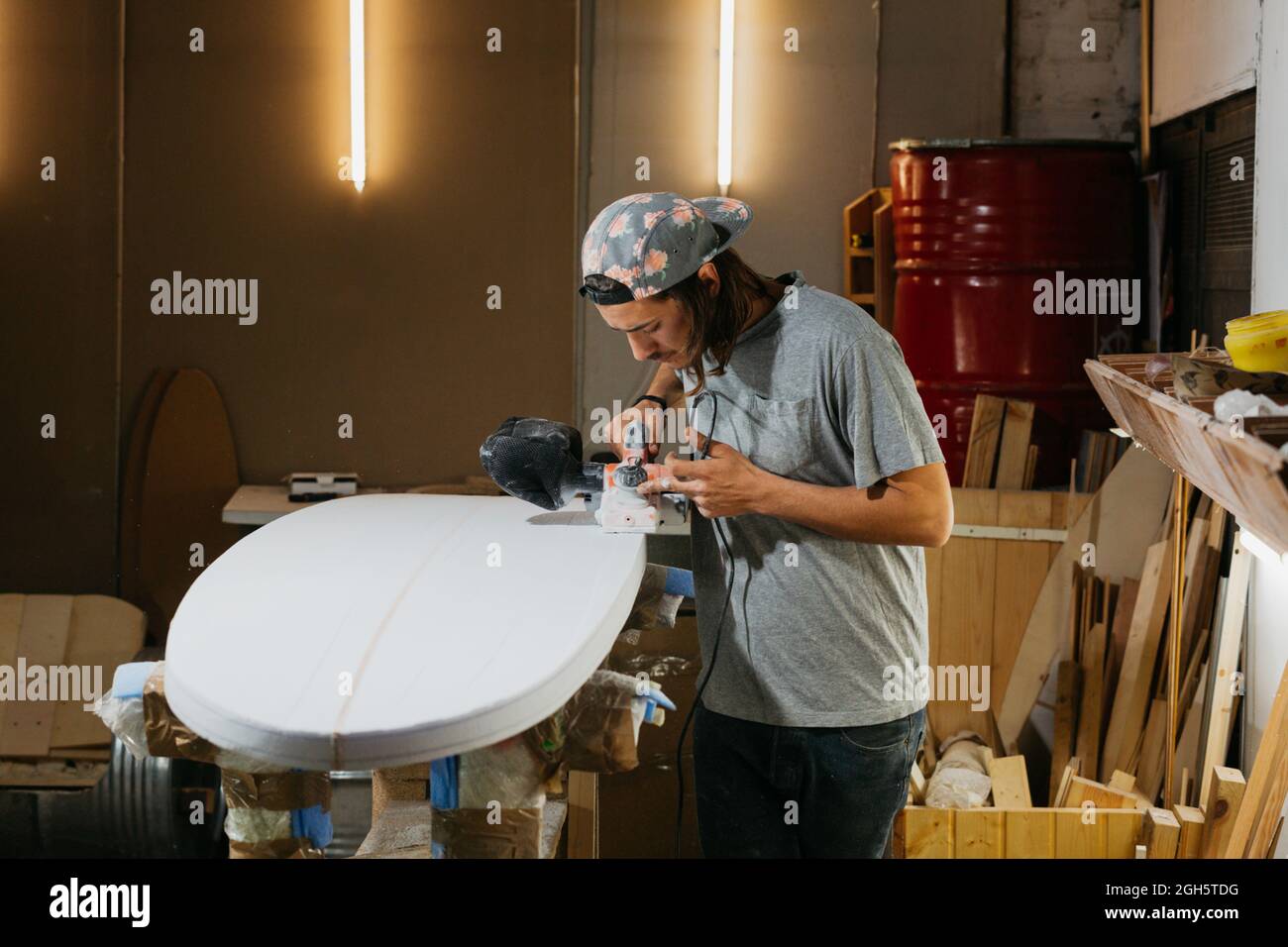 Shaper mâle à l'aide d'une fraiseuse électrique et de la surface de polissage de planche de surf en atelier Banque D'Images