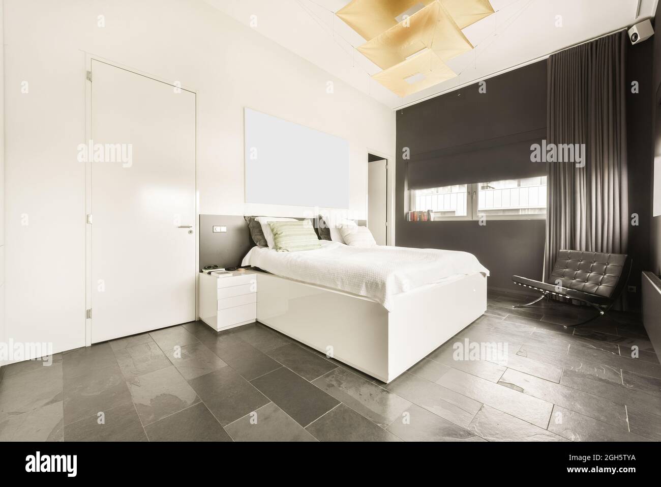 Chambre spacieuse et lumineuse avec lit Queen Size et salle de bains attenante dans un appartement moderne de style loft avec murs blancs et sol en marbre Banque D'Images