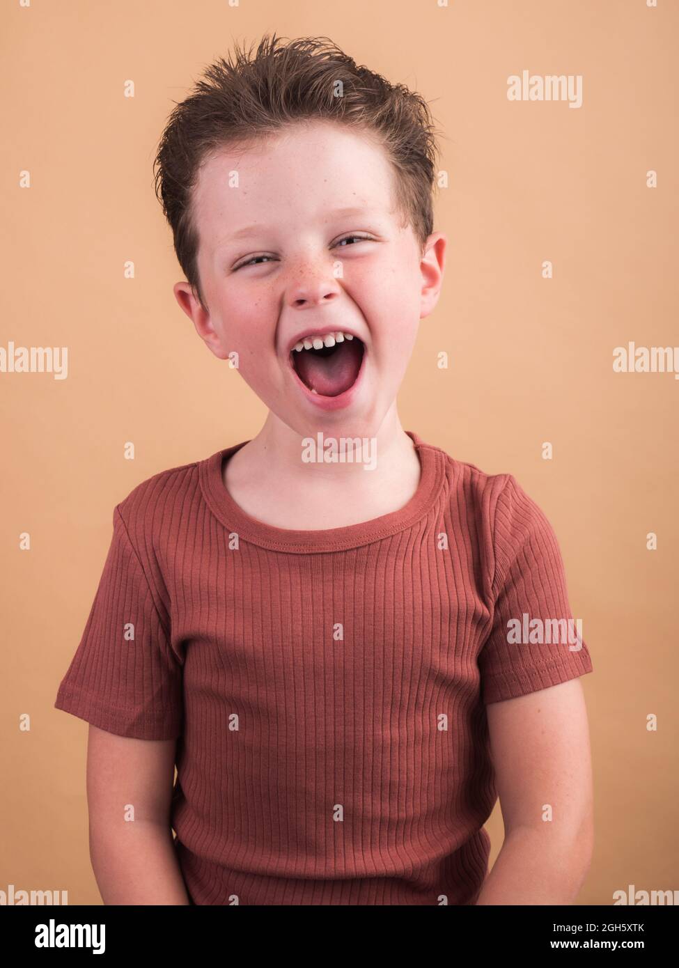 Un enfant satisfait dans des vêtements décontractés avec des cheveux bruns regardant l'appareil photo avec un sourire crasseux et une tête inclinée Banque D'Images