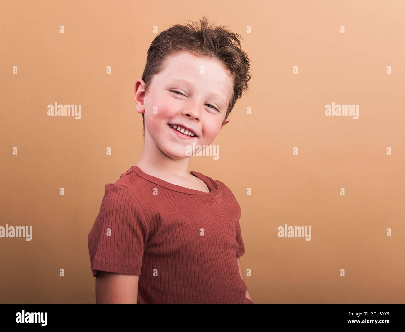 Un enfant satisfait dans des vêtements décontractés avec des cheveux bruns regardant l'appareil photo avec un sourire crasseux et une tête inclinée Banque D'Images