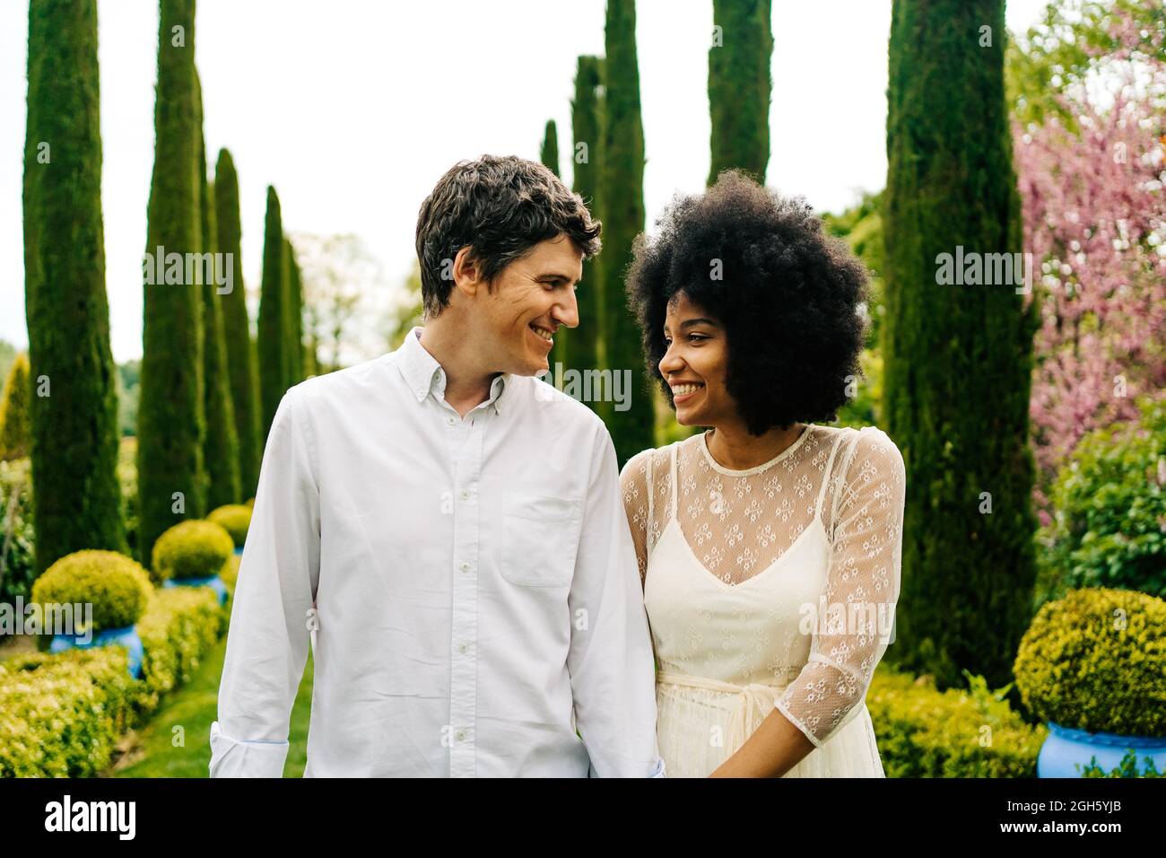 Couple multiracial joyeux tenant les mains et marchant dans le jardin tout en regardant les uns les autres Banque D'Images