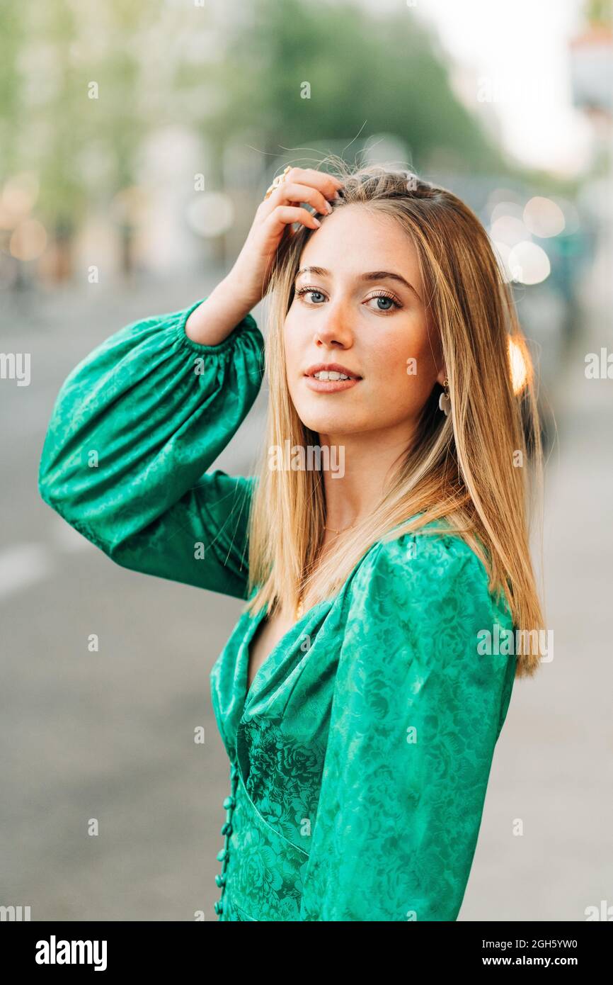 Femme insouciante dans une robe verte tendance debout avec un bras relevé  et touchant sa tête dans la rue et regardant l'appareil photo Photo Stock -  Alamy
