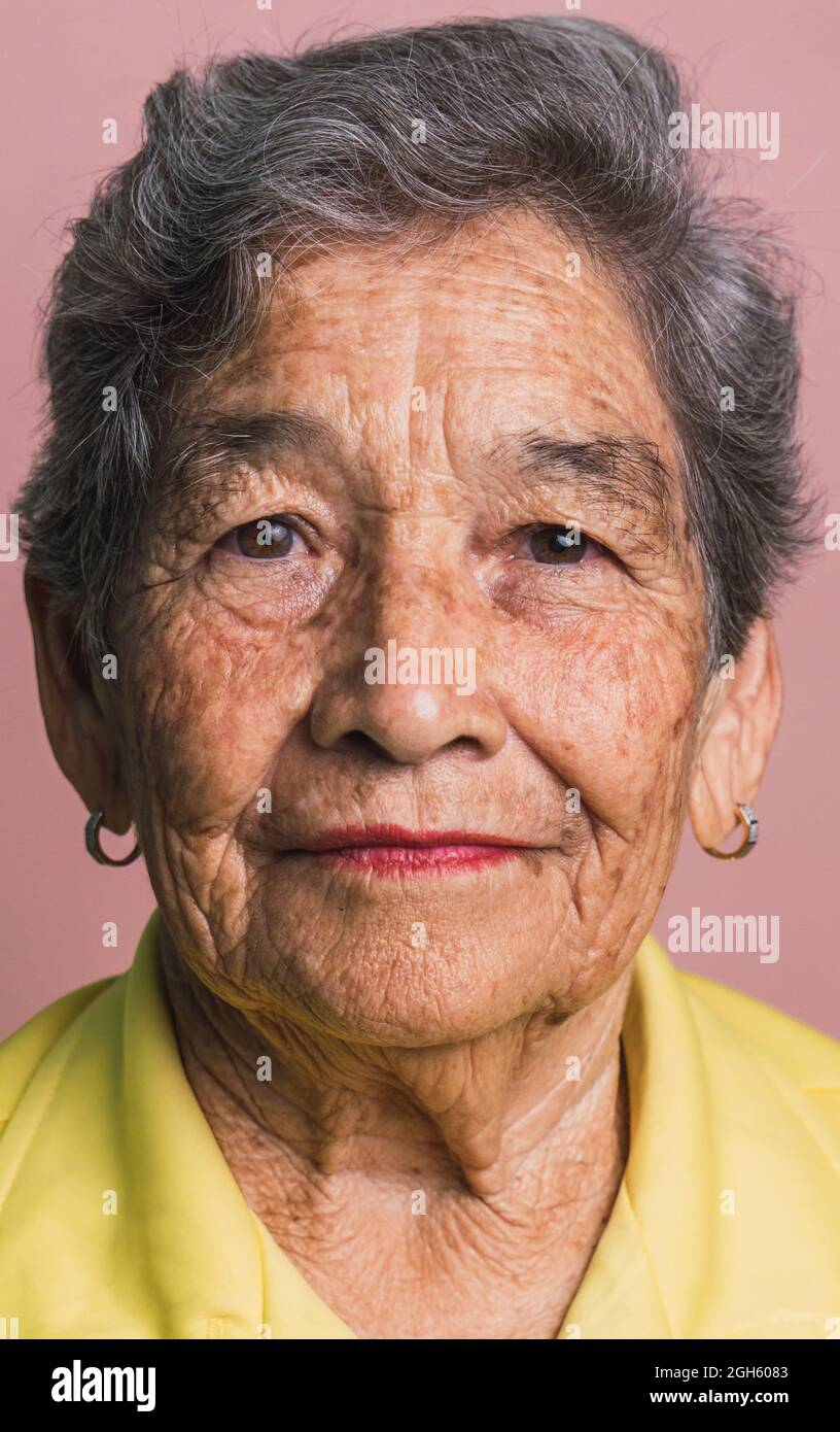 Femme âgée avec cheveux gris courts et yeux bruns regardant la caméra sur fond rose en studio Banque D'Images