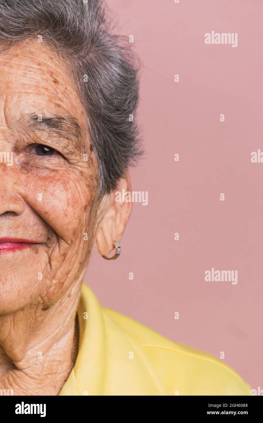 Demi-visage court de femme âgée avec cheveux gris courts et yeux bruns regardant la caméra sur fond rose en studio Banque D'Images