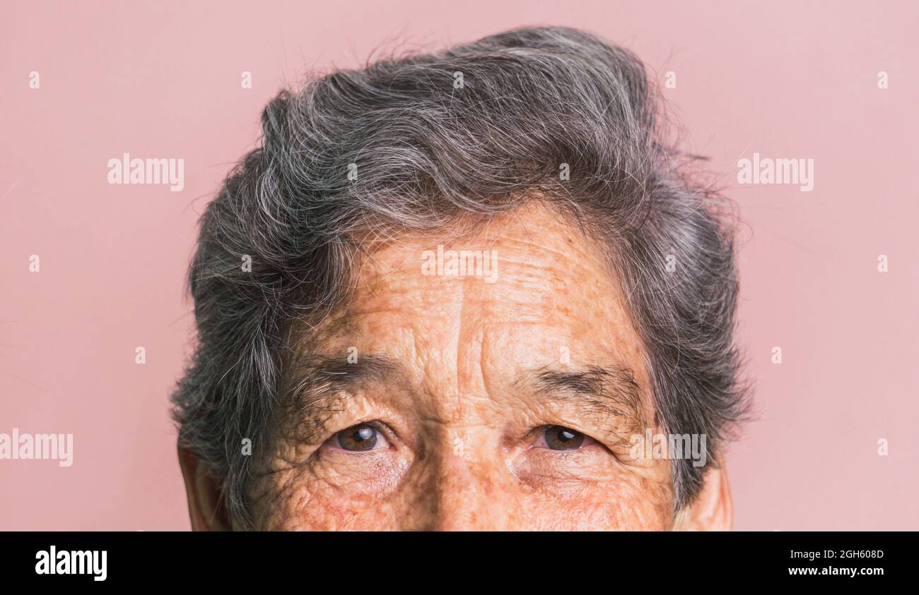 Demi-visage court de femme âgée avec cheveux gris courts et yeux bruns regardant la caméra sur fond rose en studio Banque D'Images