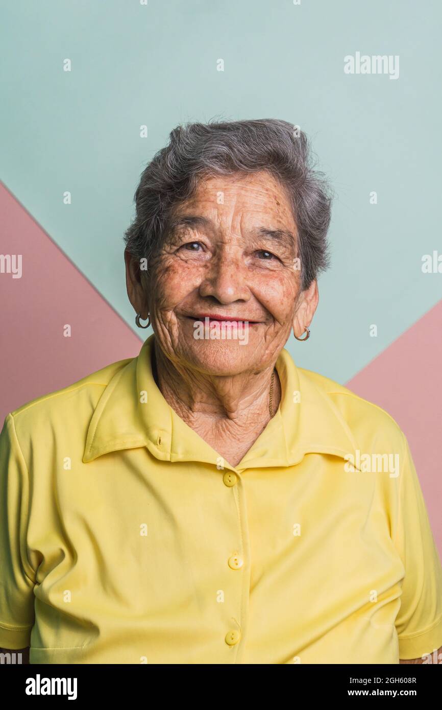 Femme âgée avec cheveux gris courts et yeux bruns regardant la caméra sur fond rose et bleu en studio Banque D'Images