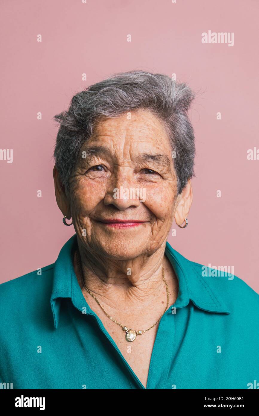 Femme âgée avec cheveux gris courts et yeux bruns regardant la caméra sur fond rose en studio Banque D'Images