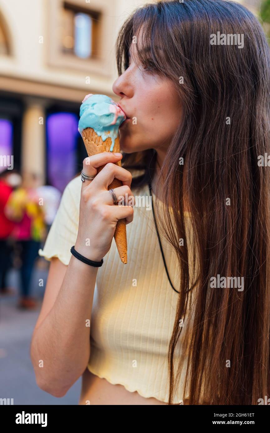 Croquer de jeunes femelles savoureuses gelato dans le cône de gaufré en ville sur fond flou Banque D'Images