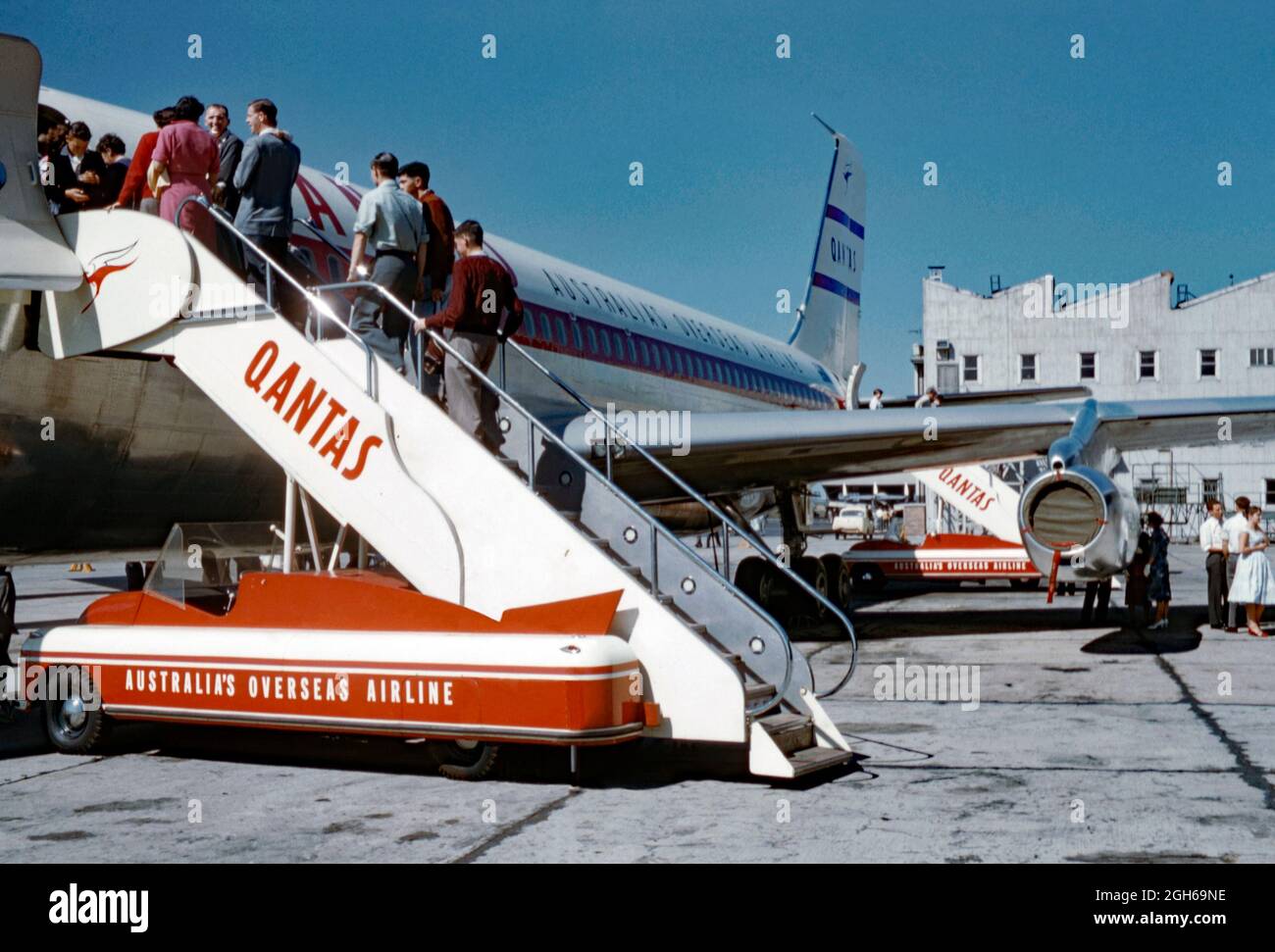 Les passagers qui embarquent dans un Boeing 707 de Qantas en 1960 au moyen d'un véhicule mobile à monter dans les escaliers. Qantas Airways Limited est le transporteur aérien de l'Australie et sa plus grande compagnie aérienne. Il s'agit de la troisième compagnie aérienne la plus ancienne au monde encore en exploitation, fondée en novembre 1920. Le logo kangourou de Qantas se trouve sur l’escalier et la queue de l’avion. Notez les courbes Art déco épurées du véhicule d'embarquement. Cette image provient d'un ancien transparent couleur Kodak amateur, une photographie vintage des années 1960. Banque D'Images