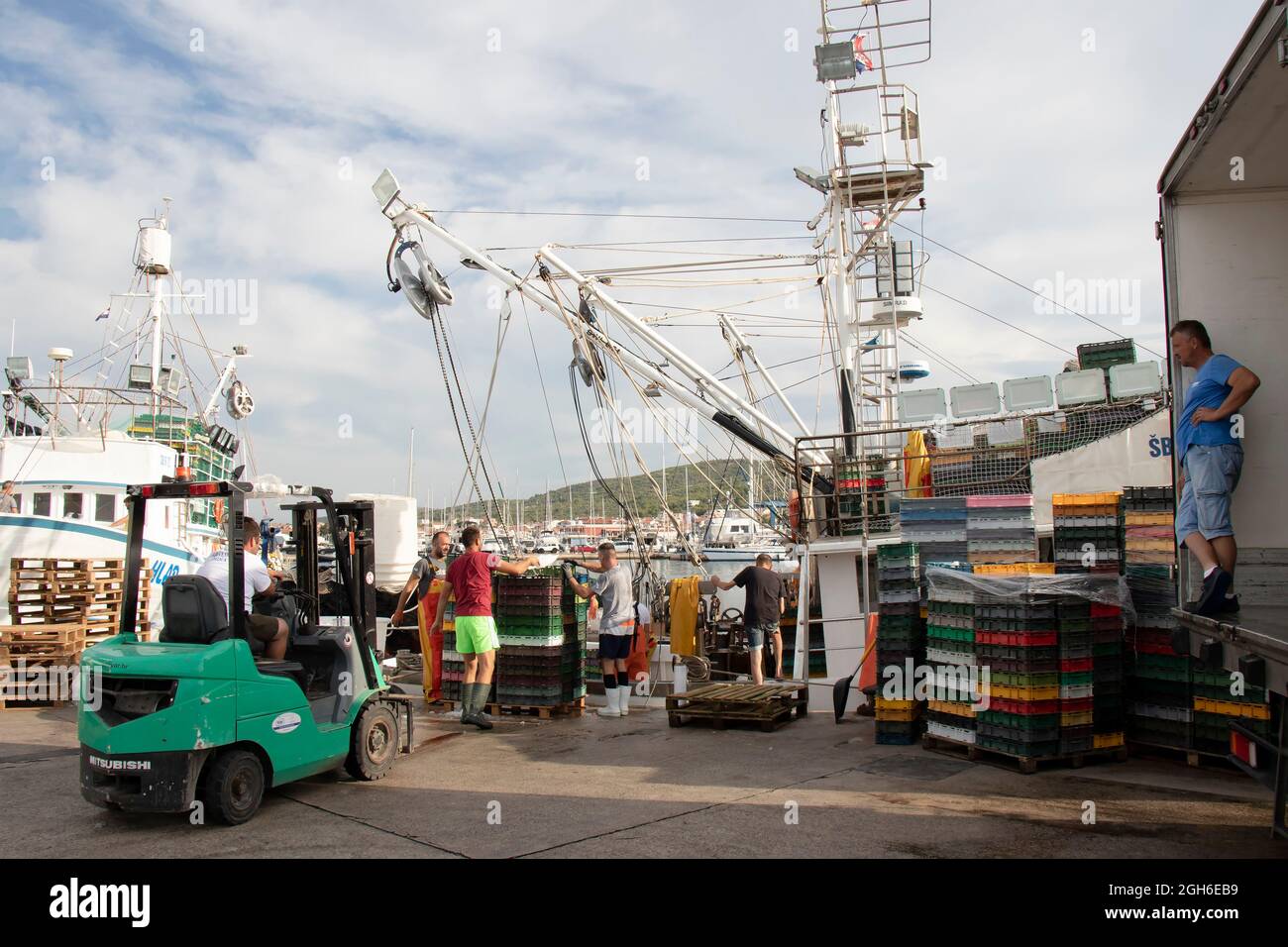 Tribunj, Croatie - 4 août 2021 : pêcheurs et travailleurs de quai chargeant des conteneurs à poisson et des caisses dans un camion à l'aide de grues à bateaux et d'un chariot élévateur à fourche Banque D'Images