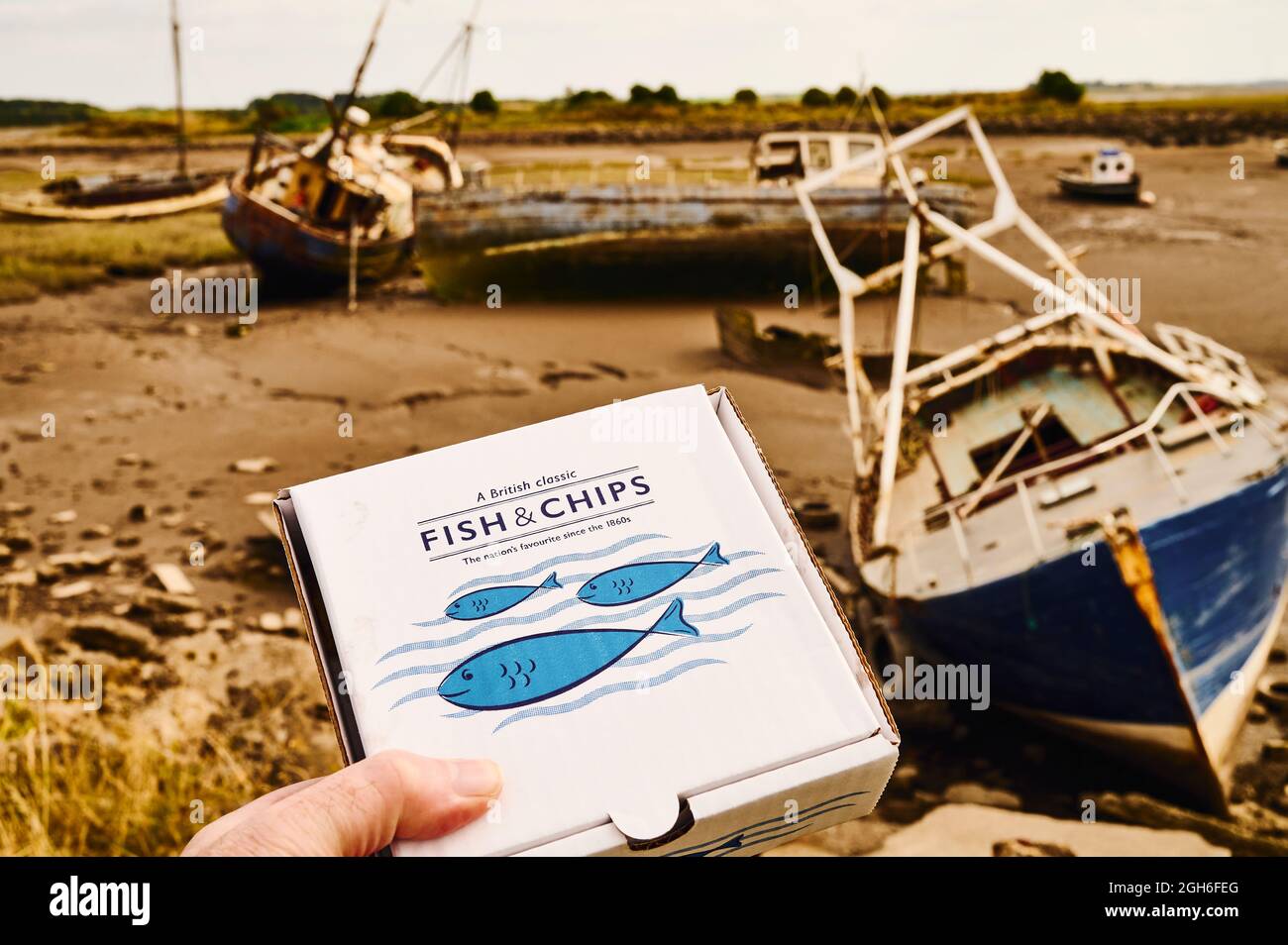 Une boîte en carton contenant du poisson et des copeaux devant les chalutiers de pêche abandonnés dans le quai à poissons de Wyre à Fleetwood Banque D'Images