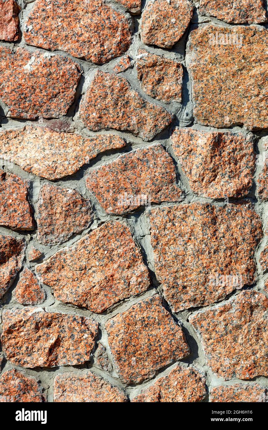 Texture d'un mur en granit rouge incrusté dans un mur en plein soleil, gros plan, haute résolution. Image verticale. Banque D'Images