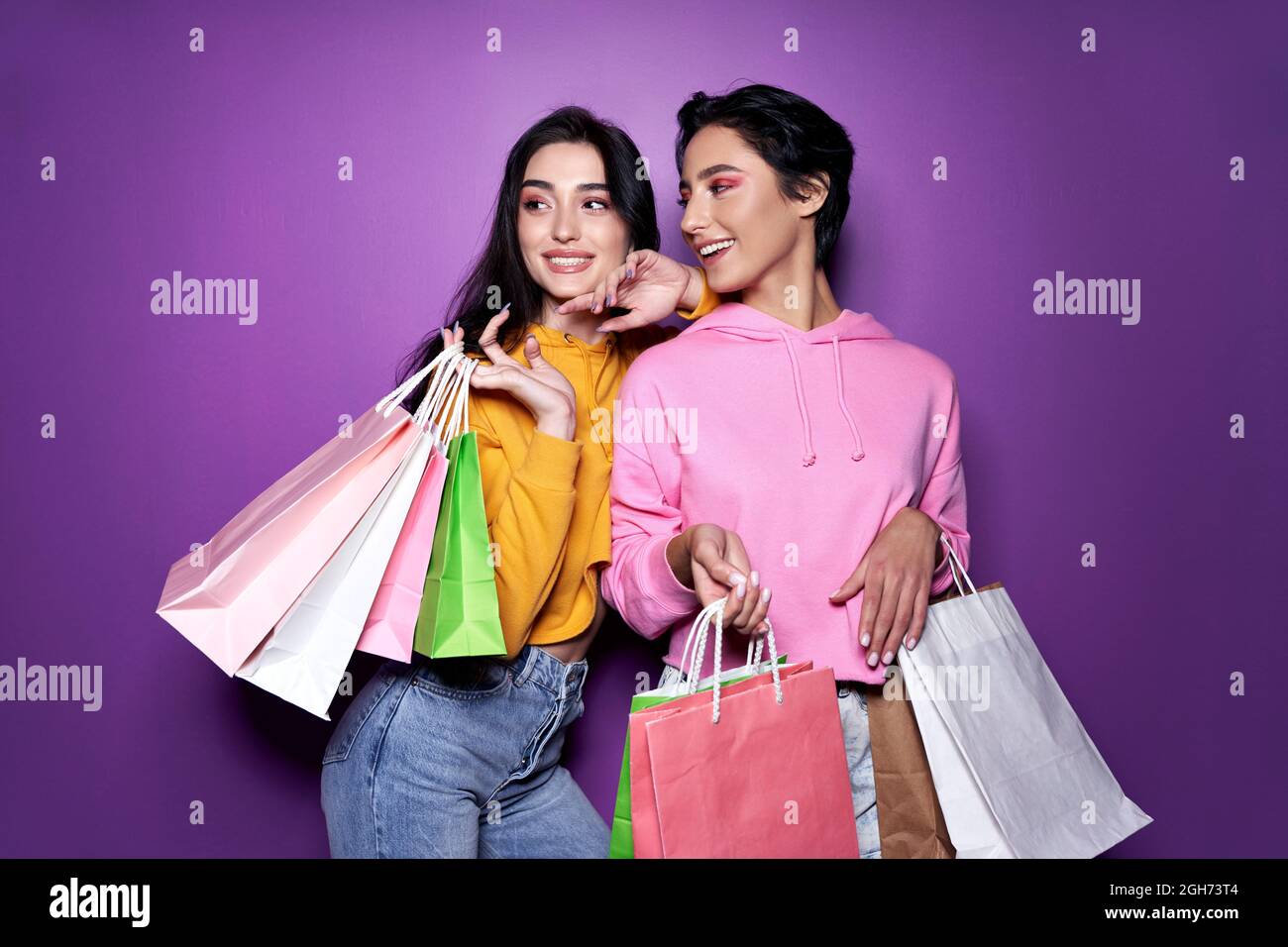 Deux amies heureuses qui tiennent des sacs d'achats sur fond violet. Banque D'Images