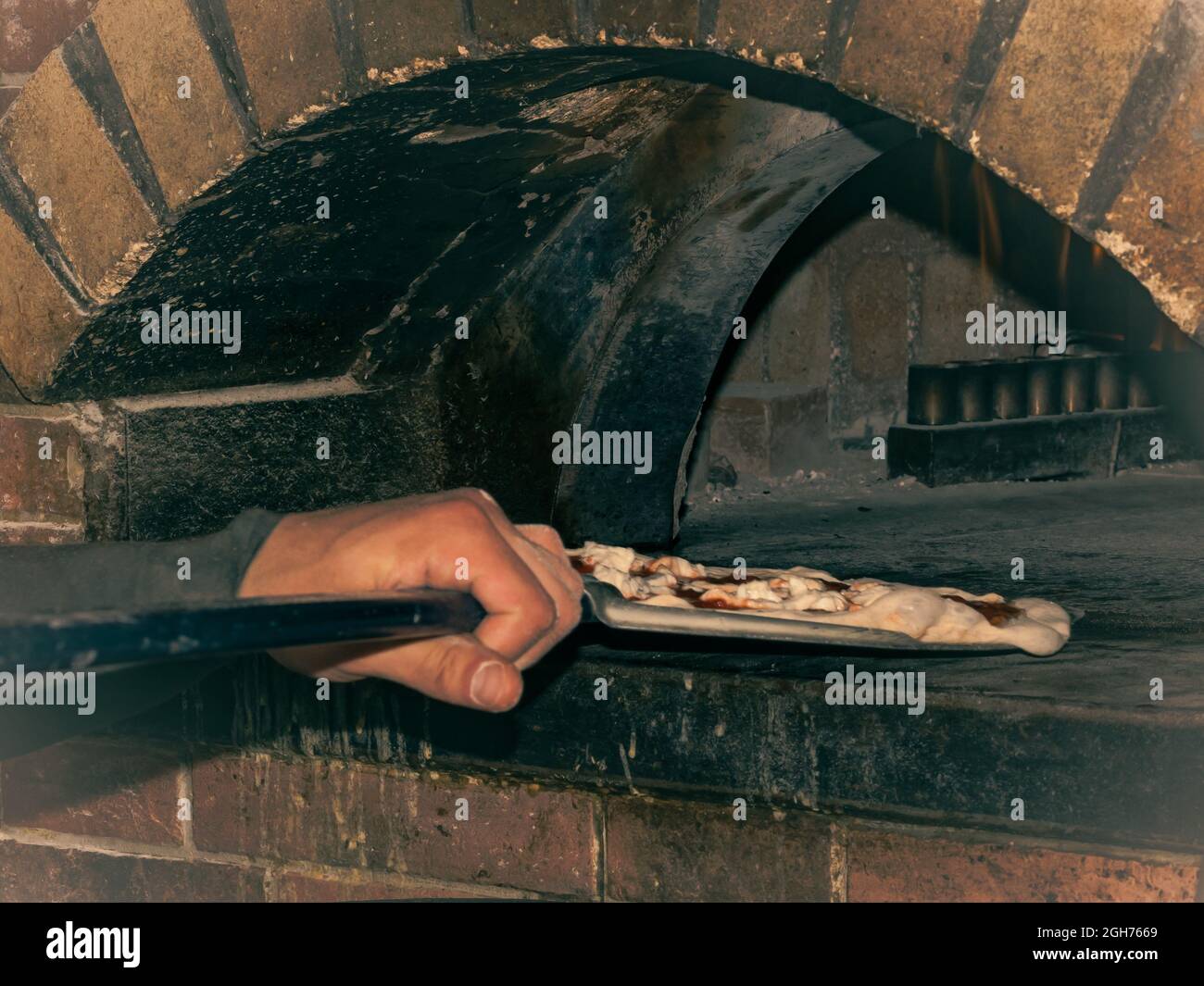 détail du bras d'un chef de pizza qui met une pizza au four Banque D'Images