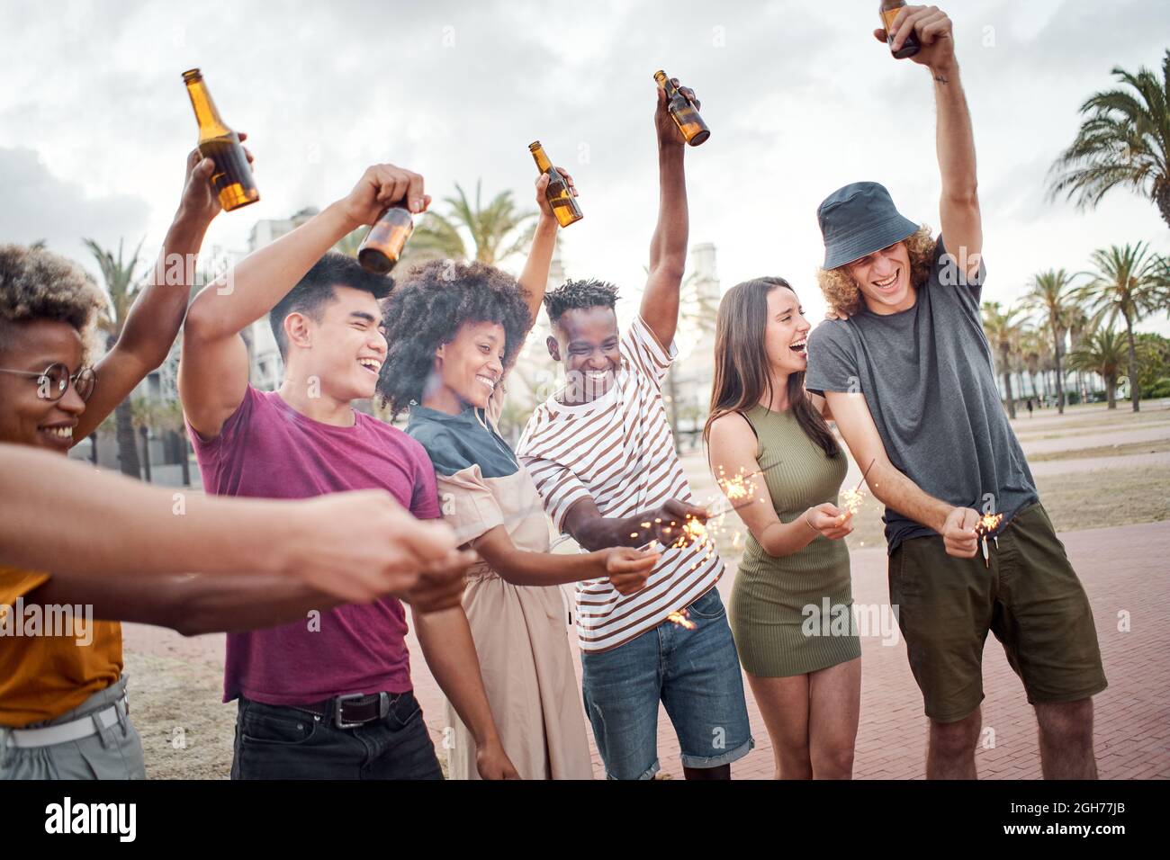 Groupe d'amis célébrant avec des sparkles et des bières. Personnes de différentes races ayant un bon moment à un festival de musique. Concept d'été, amitié Banque D'Images