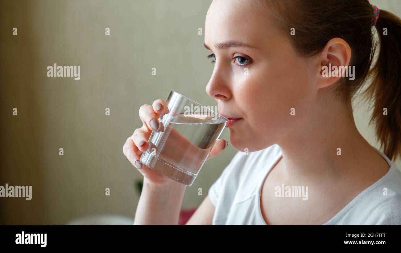 Une jeune femme boit un verre d'eau pure le matin après s'être réveillée. Bonne fille de l'adolescence maintient l'équilibre de l'eau pour la santé du corps en buvant un transparent Banque D'Images