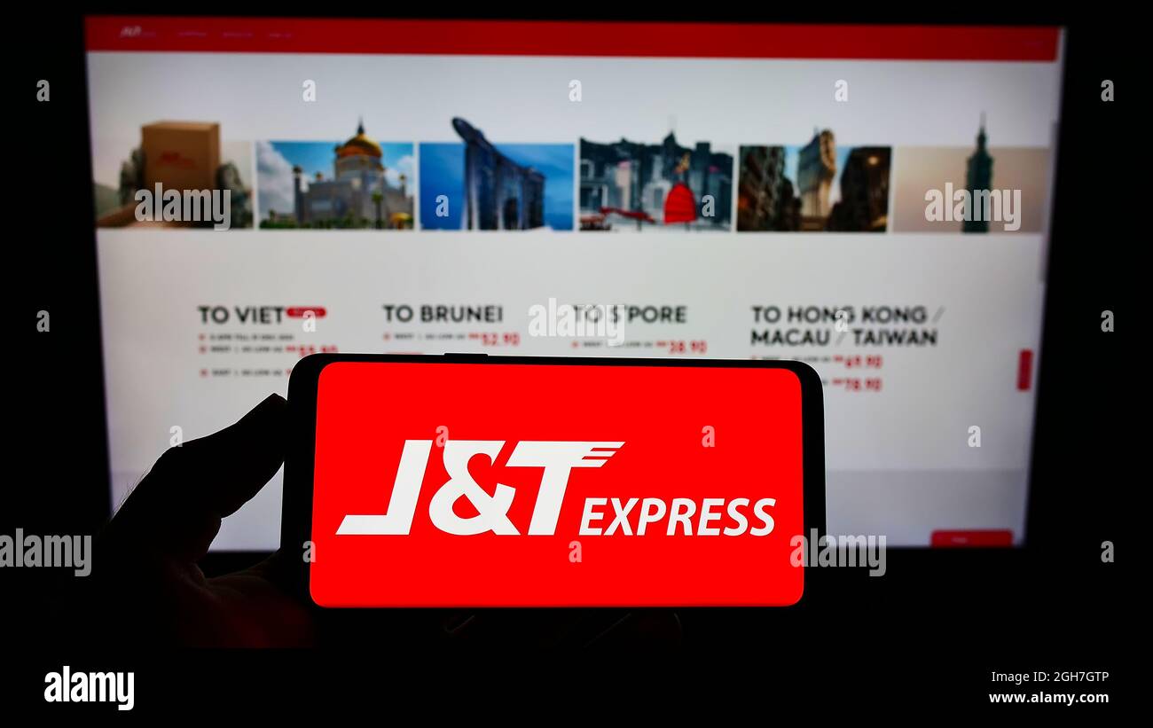Personne tenant un smartphone avec le logo de la société indonésienne PT Global Jet Express (JT) à l'écran devant le site Web. Mise au point sur l'affichage du téléphone. Banque D'Images