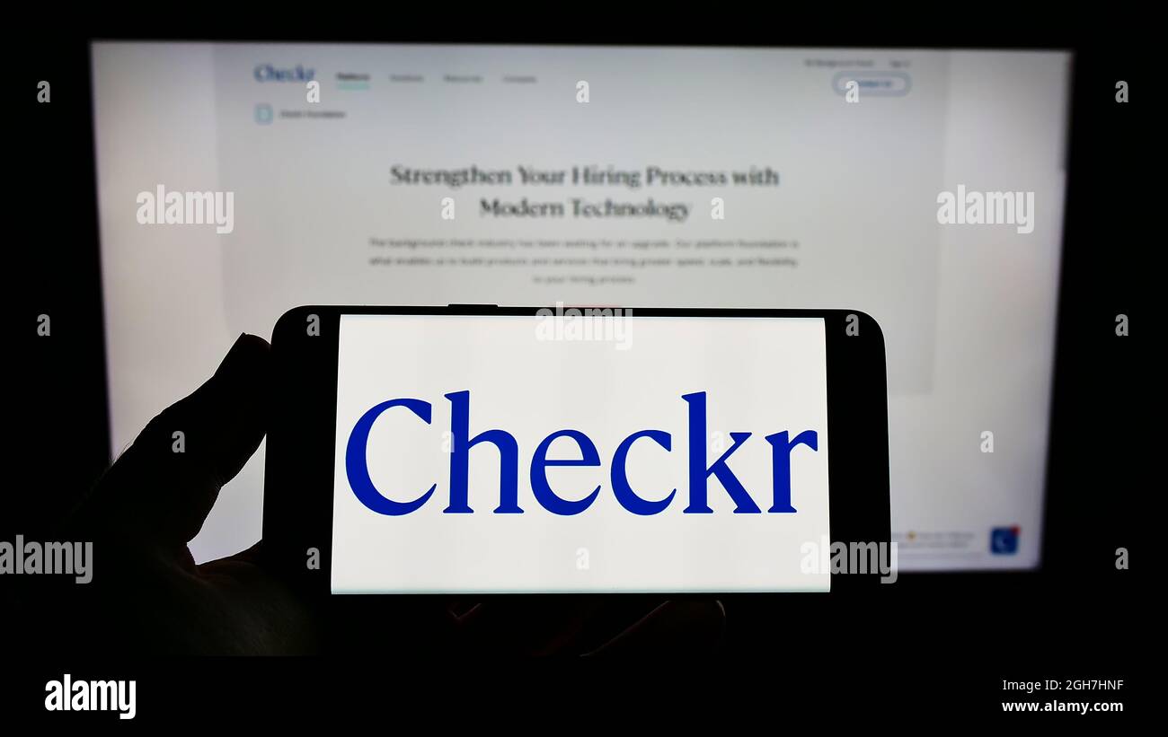 Personne tenant un smartphone avec le logo de la société de vérification des antécédents américaine Checkr Inc. À l'écran devant le site Web. Mise au point sur l'affichage du téléphone. Banque D'Images