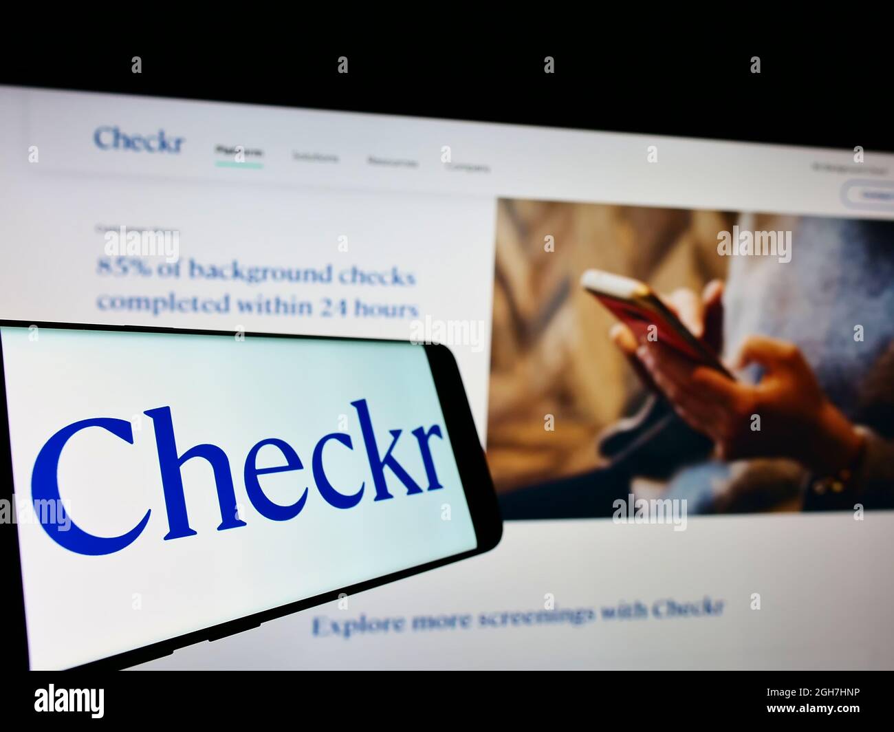 Téléphone mobile avec logo de la société de vérification des antécédents américaine Checkr Inc. À l'écran en face du site Web d'affaires. Mise au point au centre-gauche de l'écran du téléphone. Banque D'Images