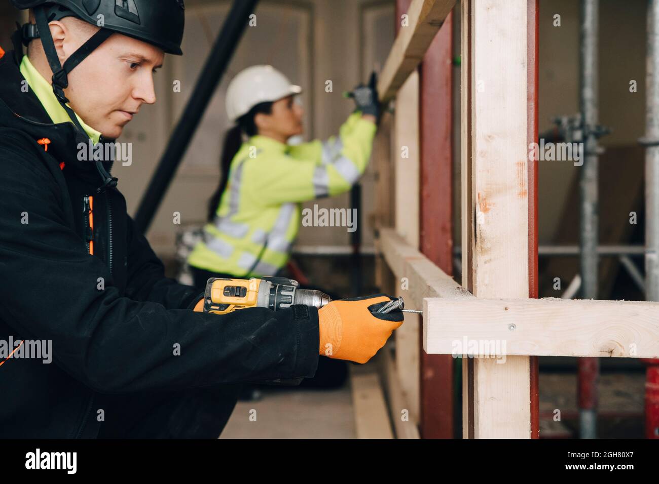 Vue latérale de l'ouvrier masculin utilisant une perceuse sur une planche en bois pendant le travail sur le chantier Banque D'Images