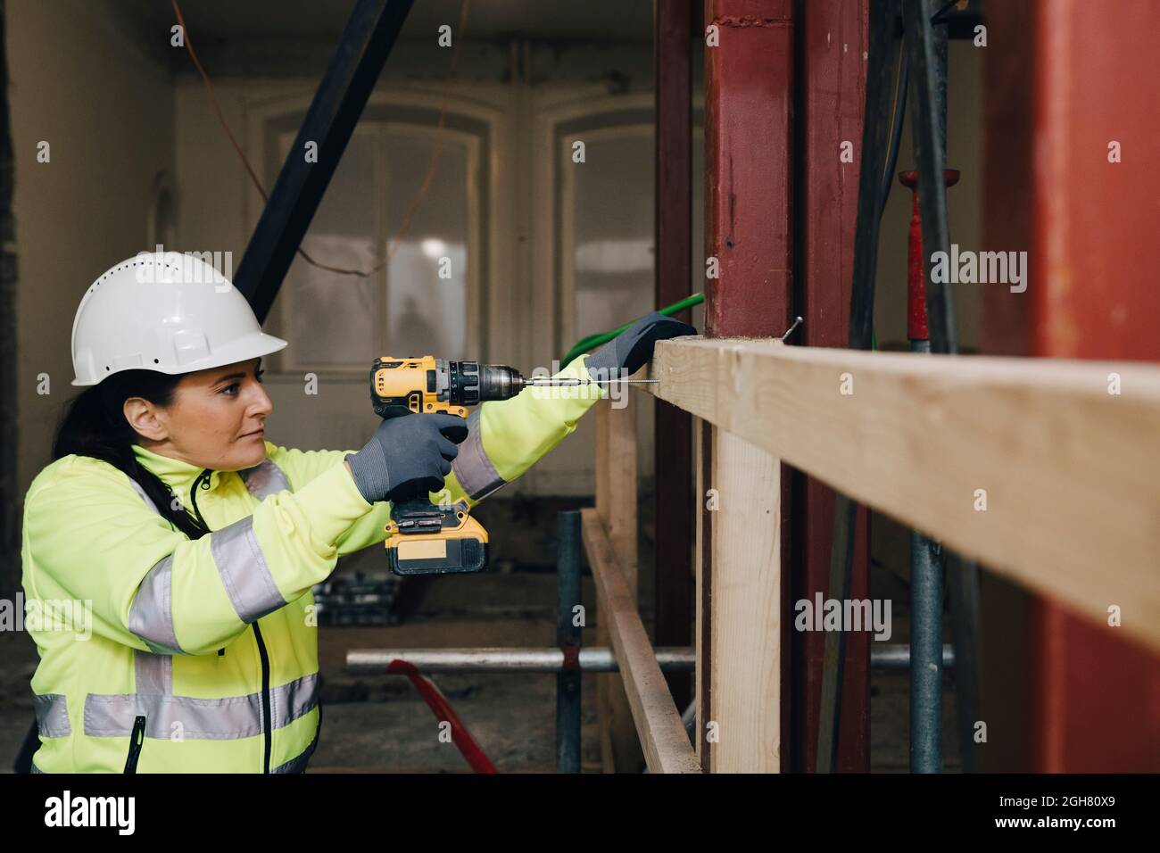 Femme utilisant une perceuse sur une planche en bois lors de travaux sur le chantier de construction Banque D'Images
