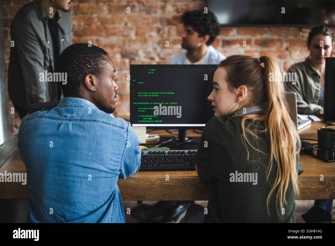 Une jeune femme hacker parle avec un collègue tout en codant sur un ordinateur au bureau Banque D'Images