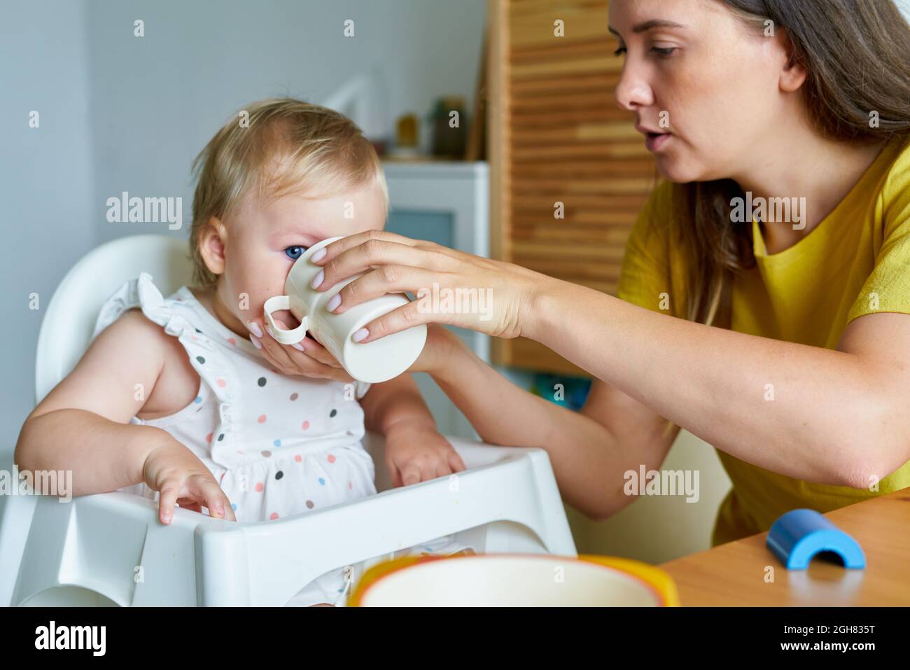 Mère nourrissant sa fille avec une préparation pour bébé dans une tasse. Une alimentation saine. Garde d'enfants Banque D'Images
