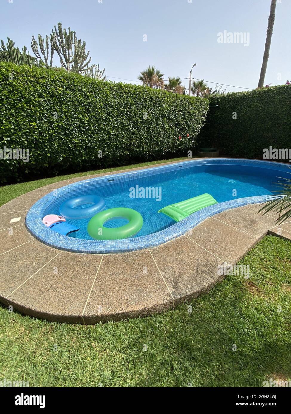Piscine extérieure avec flotteurs verts et bleus entourés d'une clôture en herbe Banque D'Images